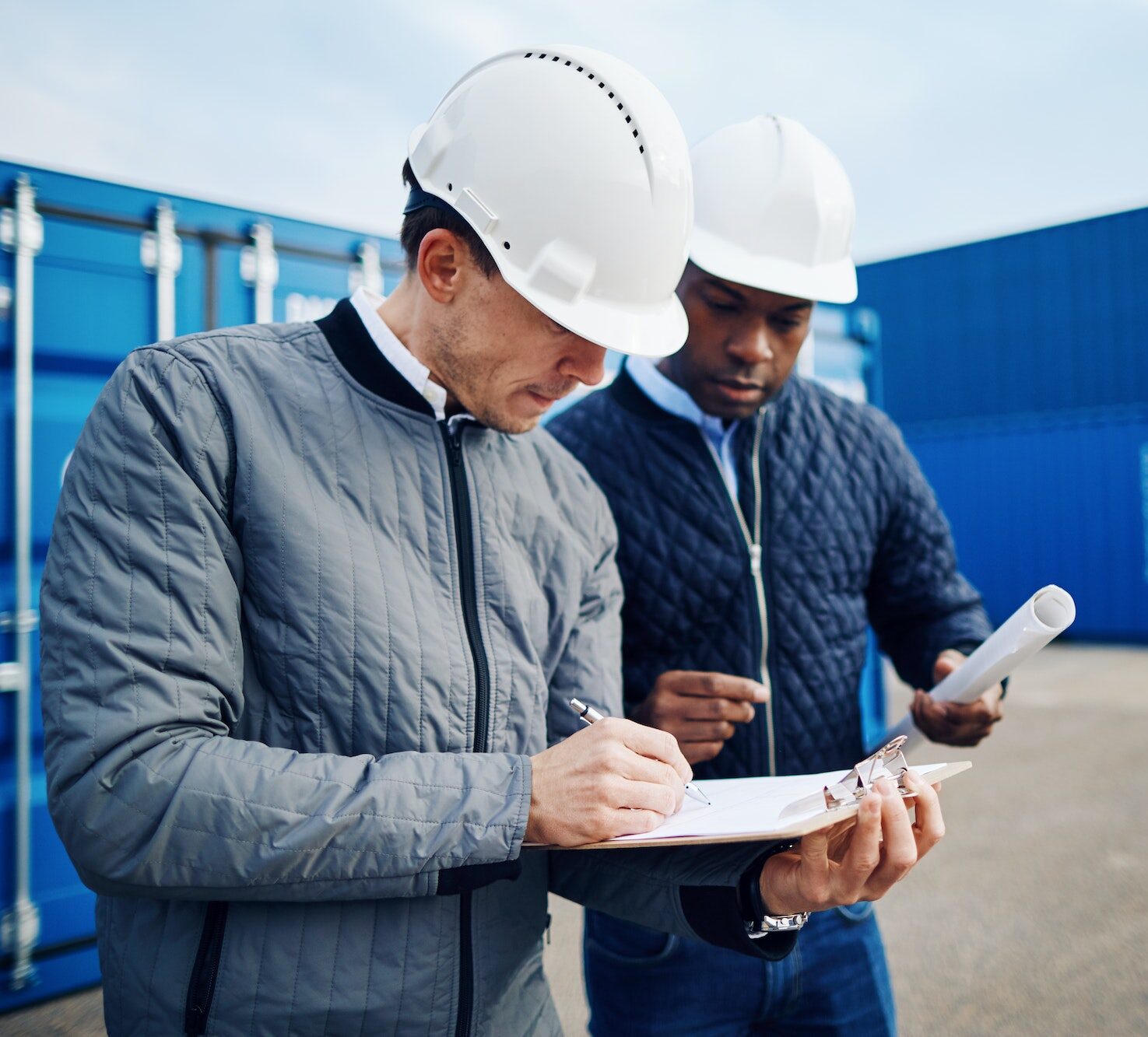Two engineers standing in a shipping yard discussing logistics